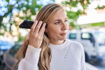 Canvas Print - Young blonde woman listening audio message by the smartphone with serious expression at street