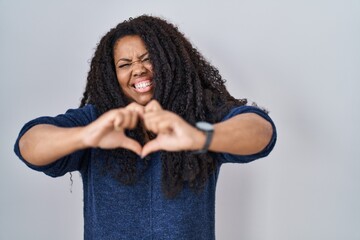 Wall Mural - Plus size hispanic woman standing over white background smiling in love doing heart symbol shape with hands. romantic concept.