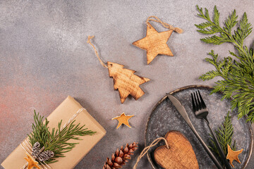 Wall Mural - Winter holiday table setting on gray background. Dark plate, cutlery, gift box and Christmas decor. Winter holiday mood, Christmas, New Year composition. Flat lay, top view with copy space