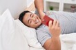 Young chinese man using smartphone lying on bed at bedroom