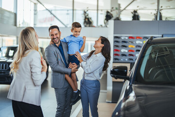 Young happy family and male salesperson using digital tablet in a car showroom. Happy young family buying their new car. Young happy family and female salesperson using digital tablet