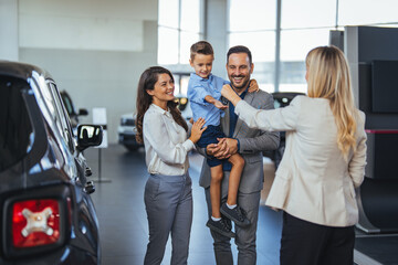 Happy family holding the keys of their new car at the dealership. Saleswoman at car dealership center helping family to choose new family vehicle.