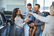 Happy family choosing new car, salesman showing them luxury auto at automobile dealership store. Customers selecting vehicle, consulting manager at modern showroom shop