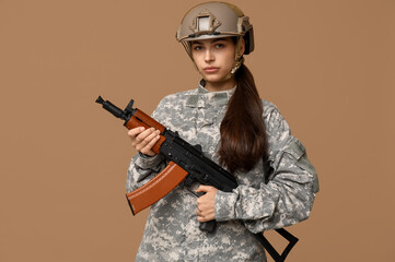 Confident young female soldier with assault rifle on beige background