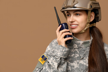 Wall Mural - Confident young female soldier speaking into military radio on beige background, closeup