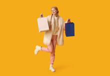 Beautiful Young Happy Woman In Warm Winter Clothes With Shopping Bags On Yellow Background