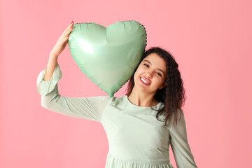 Wall Mural - Happy young woman with heart shaped air balloon on pink background