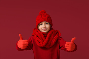 Canvas Print - Cute little happy boy in winter clothes showing thumbs-up gesture on red background