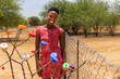 village young african girl with red dress standing in the yard behind a tree with colorful bottle caps