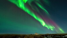 Time lapse shot of flickering green and purple aurora borealis at night sky of Iceland with parking car on road - wide shot