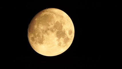 Wall Mural - A glowing golden huge full moon seen from earth through the atmosphere against a starry night sky. A large full moon moves across the sky, the moon moving from the bottom left frame to the top right.