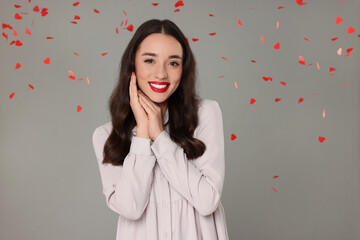 Poster - Beautiful young woman under falling heart shaped confetti on grey background