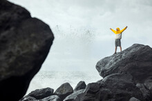 Man With Arms Raised Standing On Rock Near Splashing Waves Of Sea