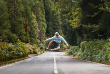 Carefree Young Man Jumping On Road In Front Of Trees