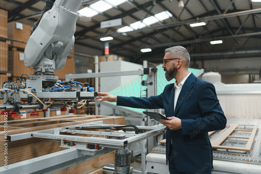 Male engineer in modern industrial factory, checking robotic arm ...