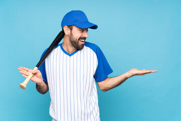 Wall Mural - Young man playing baseball over isolated blue background holding copyspace with two hands