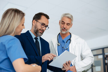 Pharmaceutical sales representative talking with doctors in medical building, presenting them new product on tablet, business talk. Hospital director consulting with healthcare staff.