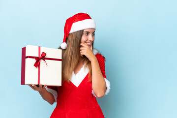 Wall Mural - Young caucasian woman dressed as mama noel holding gift isolated on blue background thinking an idea and looking side