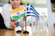 Unrecognizable unfocused woman preparing room for international negotiations and communication discussions of leaders. Lady sets miniatures of flags of Greece and India on table.