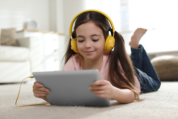 Wall Mural - Cute little girl with headphones and tablet listening to audiobook at home