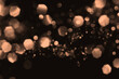 Peach fuzz blurred abstract bokeh lights on black background. Snowy shiny glitter sparkle stars for celebrate