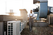 © sofiko14 - Concentrated bearded man wearing uniform holding toolkit and using digital tablet on factory. Caucasian professional craftsman walking by air conditioners and inspecting area on roof.
