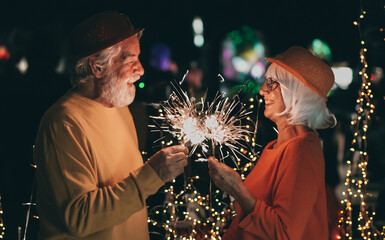 Wall Mural - Celebrate event new year for couple of nice senior people sparkling lights - cheerful elderly caucasian man and woman having party by night. Happiness lifestyle for mature retired people