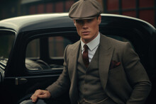 A Handsome Gentleman Dressed In A 20s Fashion Style Suit And Flat Cap Stands In Front Of The Black Vintage Car. Portrait Of The Retro Business Man, Medium Shot.