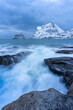 Waves crashing against rocks in the arctic sea with snowcapped mountains in the background