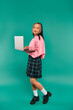 © LIGHTFIELD STUDIOS - pleased asian girl in pink sweatshirt using laptop while standing on turquoise backdrop, networking