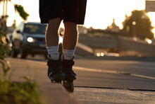 A Man Rides Roller Skates On The Paved.walkway At Sunset On City Roads In Summer. Rollers Close-up In The Backlight Of The Sun.