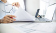 © Lek - Close-up shot, business consultant holding pen reviewing documents and contact customer via laptop to give advice about business contracts and various important documents before investing in business