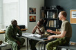 © pressmaster - Group of happy young intercultural students having discussion at break while sitting in front of each other by desk in classroom