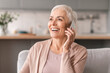 © Prostock-studio - Smiling mature woman talking on cellphone sitting on sofa indoor