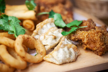 Wall Mural - Gyoza dumplings background. Deep fried cripsy food. Fried chicken wings. Onion rings on wooden plate. Plate of deep fried food. Patry dish of food snacks. Family sharing plate of food.