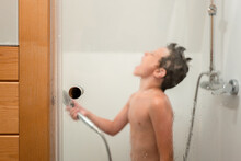 Boy holding hand shower while taking bath in bathroom