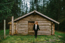 Woman Standing By A Rustic Log Cabin In The Woods