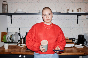 Waist up portrait of bald young woman looking at camera with confidence in kitchen, with flash