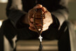 Closeup of priest holding wooden rosary beads and praying in ethereal sunlight, copy space