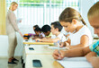 © JackF - Positive girl sits at a desk next to diligent elementary school students