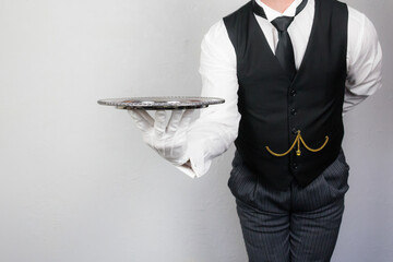 Wall Mural - Portrait of Butler or Waiter in Black Vest or Waistcoat Holding Silver Serving Tray. Concept of Service Industry and Professional Hospitality.