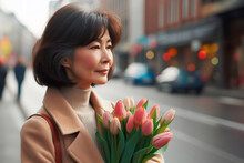 Happy Middle-aged Woman With A Bouquet Of Tulips Walks Along City Street.