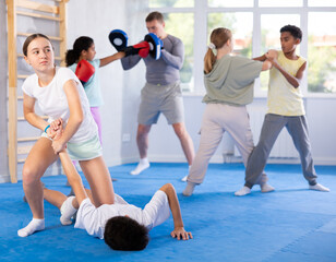 Wall Mural - Tweens taking self-defense classes at training center. Determined girl applying armlock technique to face-down boy in mock fight