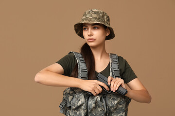 Wall Mural - Confident young female soldier with handgun on beige background