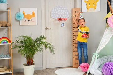 Wall Mural - Cute shocked little boy with Birthday cake measuring height in decorated room