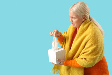 Poster - Sick mature woman taking tissue from box on blue background