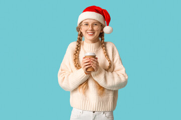 Wall Mural - Young happy woman in Santa hat with paper cup of tea on blue background