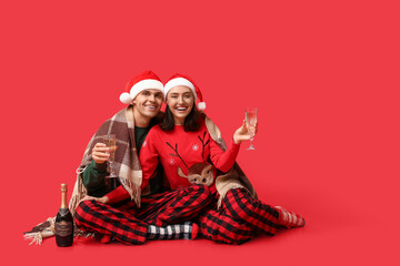 Sticker - Happy young couple in Christmas pajamas and with champagne on red background