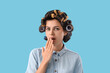 Surprised young woman with hair curlers on blue background