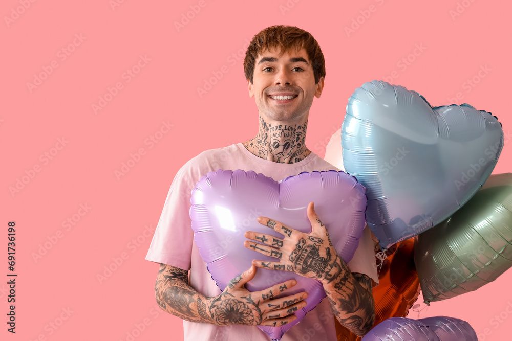 Happy young man with heart shaped air balloons on pink background